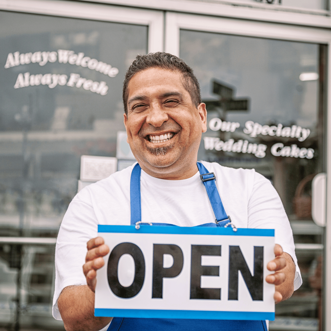 A Canadian small business owner holding Open sign board in front of his cake shop after happily signing up with DFSIN Toronto West insurance